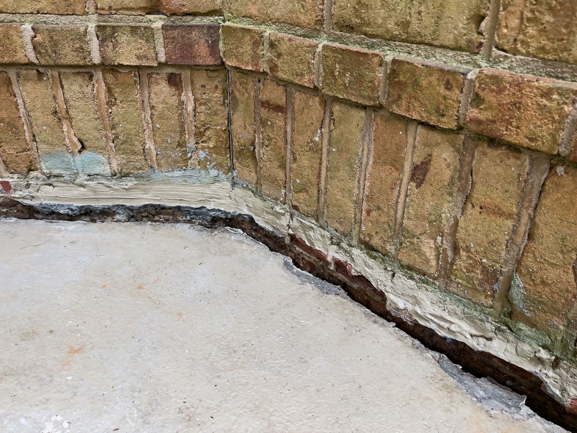 Crack and separation between concrete slab and brick wall at the base of a building foundation.