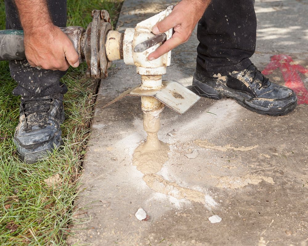 Man does mudjacking work in Lakeville, MN, on a part of concrete next to grass, representing the ser