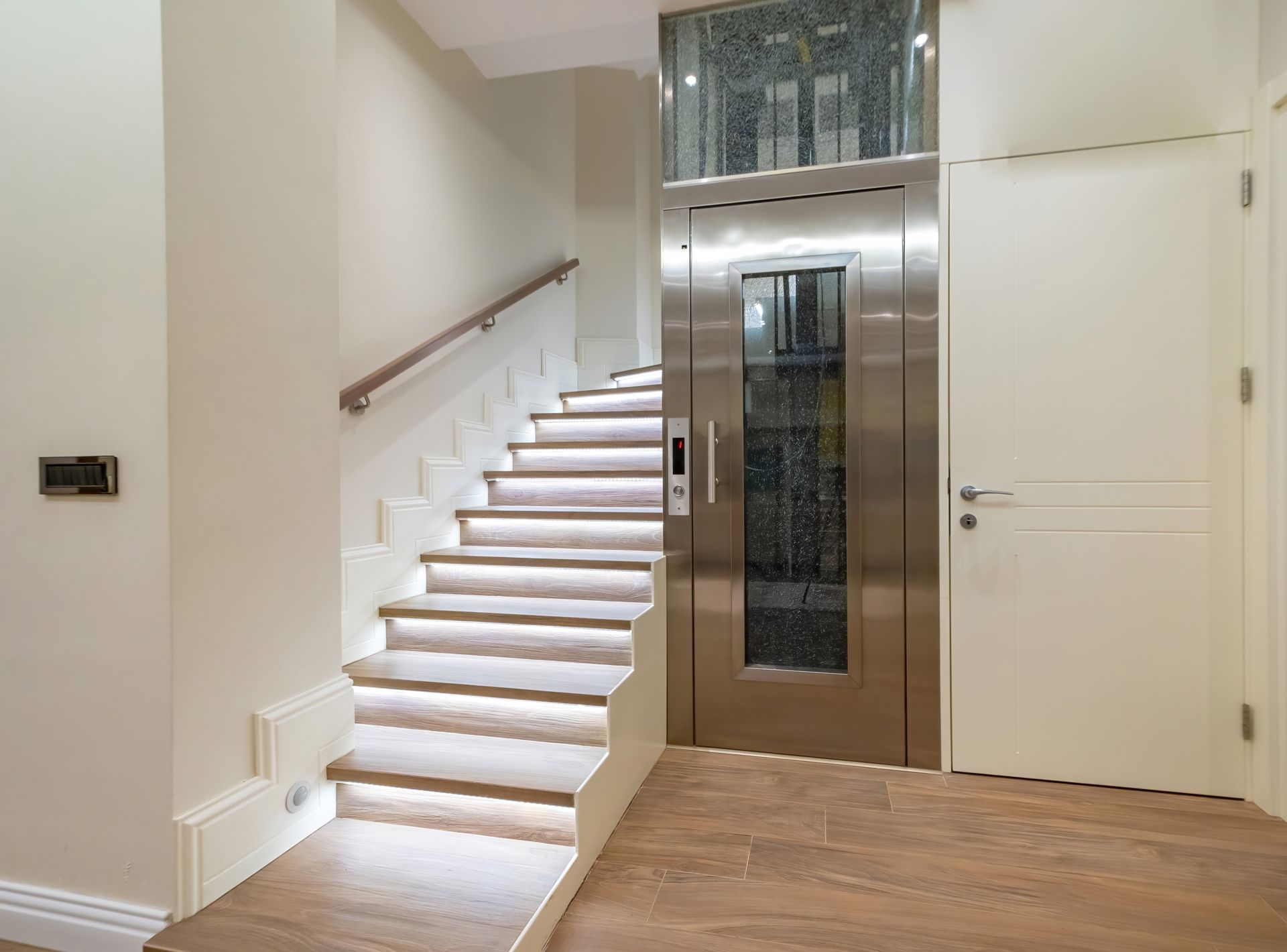 Staircase with LED lighting next to a stainless steel elevator