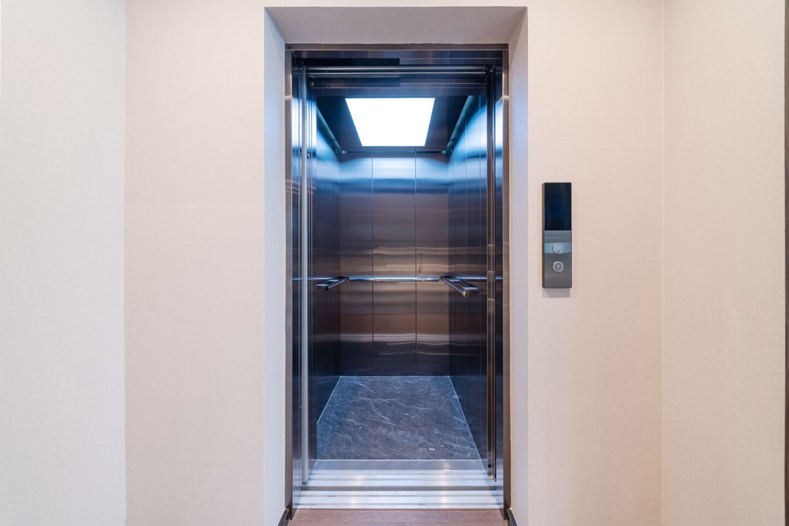 Open elevator with stainless steel walls and a dark floor, framed in a neutral-colored wall