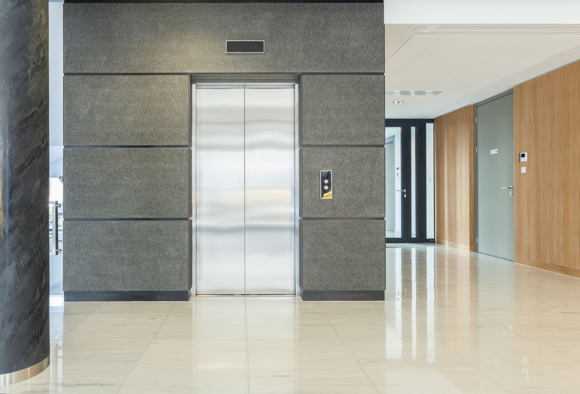 Elevator with closed metal doors in a modern building lobby, textured gray wall, beige tile floor