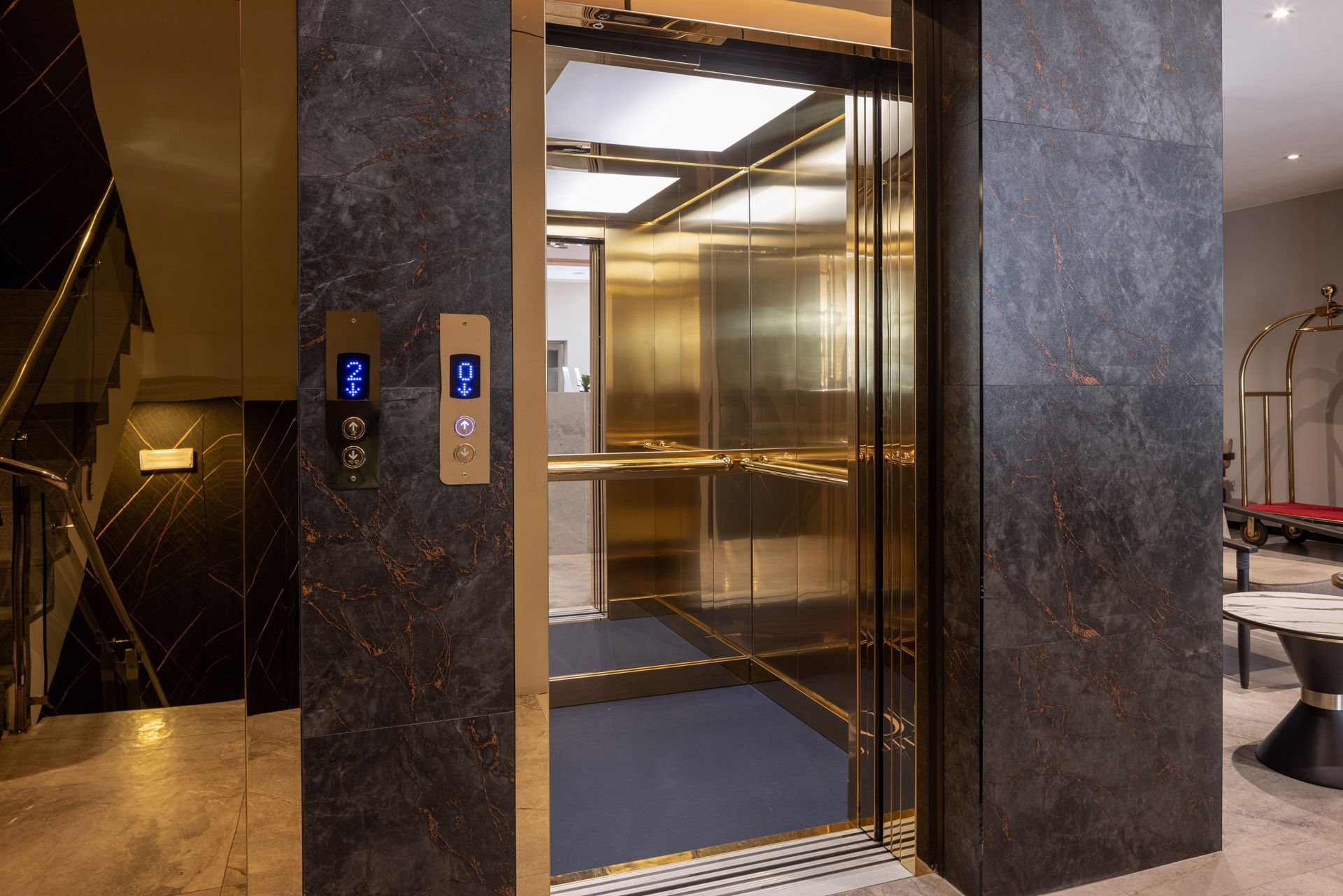 A luxurious elevator with gold accents, open, in a dark granite-walled lobby