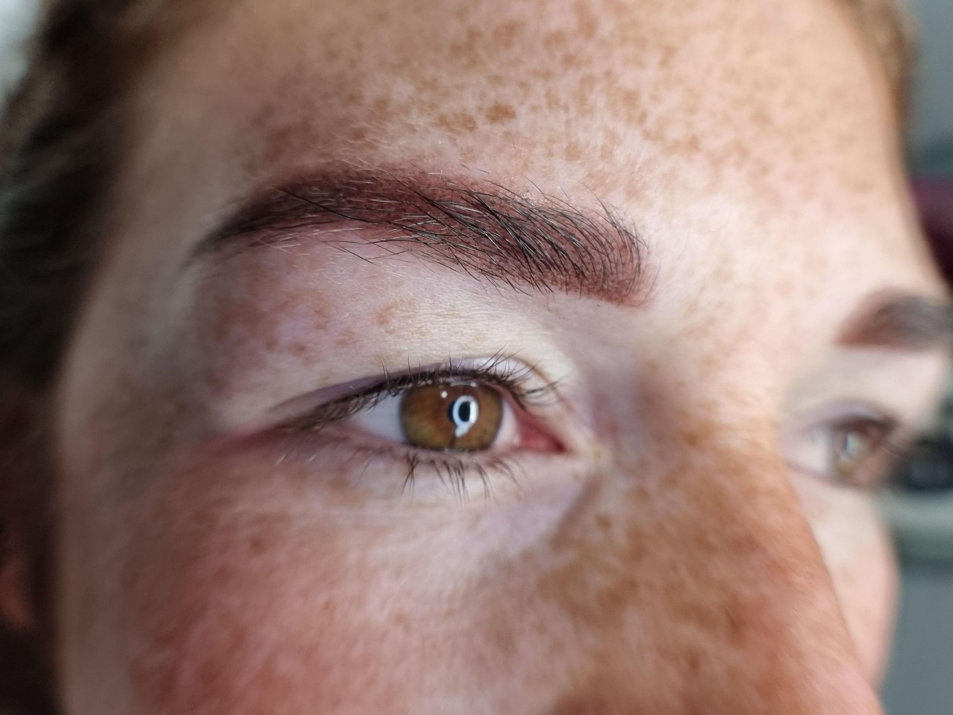 Eine Nahaufnahme des Auges und der Augenbrauen einer Frau mit Sommersprossen.