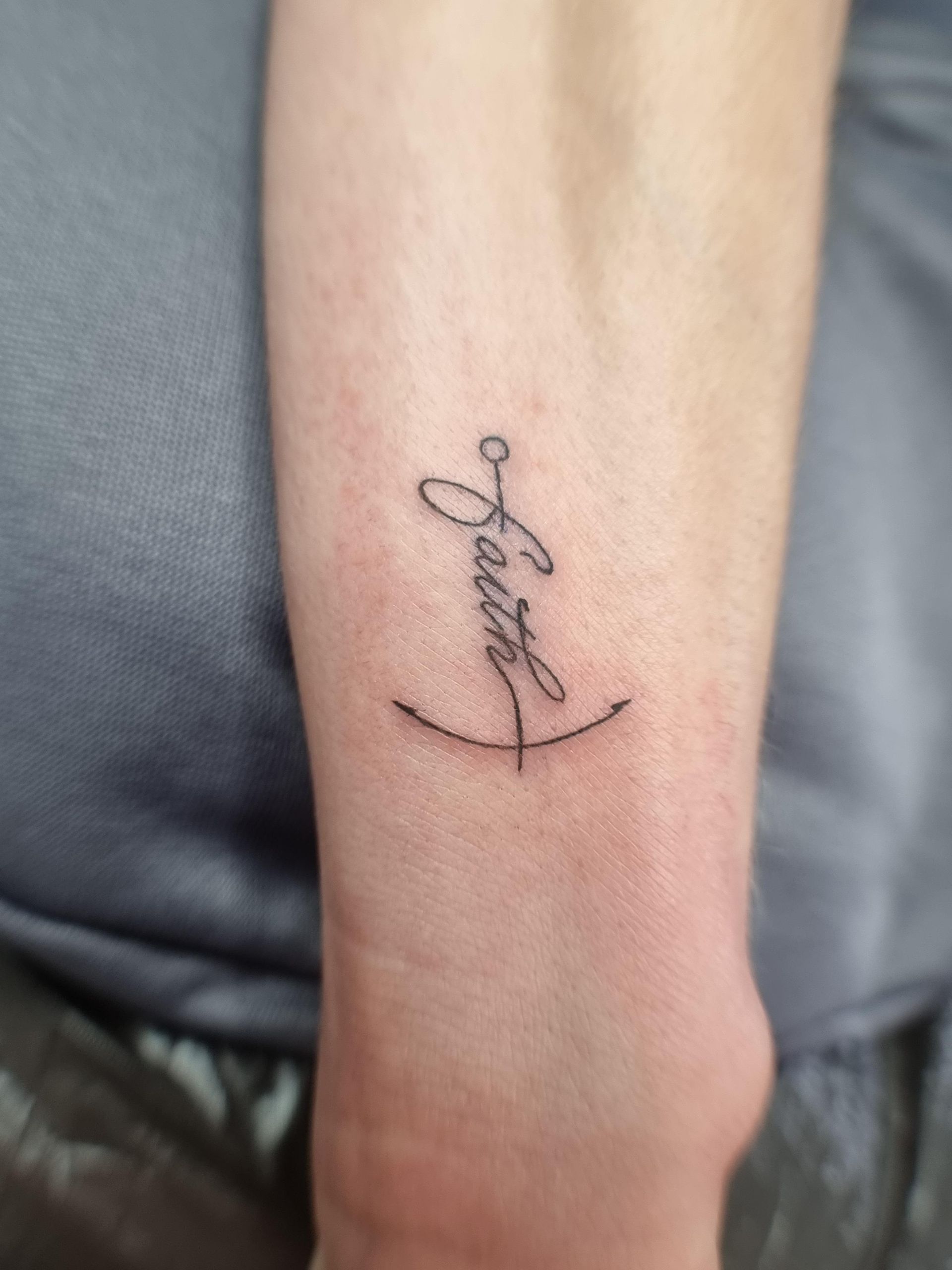 Eine kleine Tätowierung mit dem Wort „Glaube“ am Handgelenk einer Person.