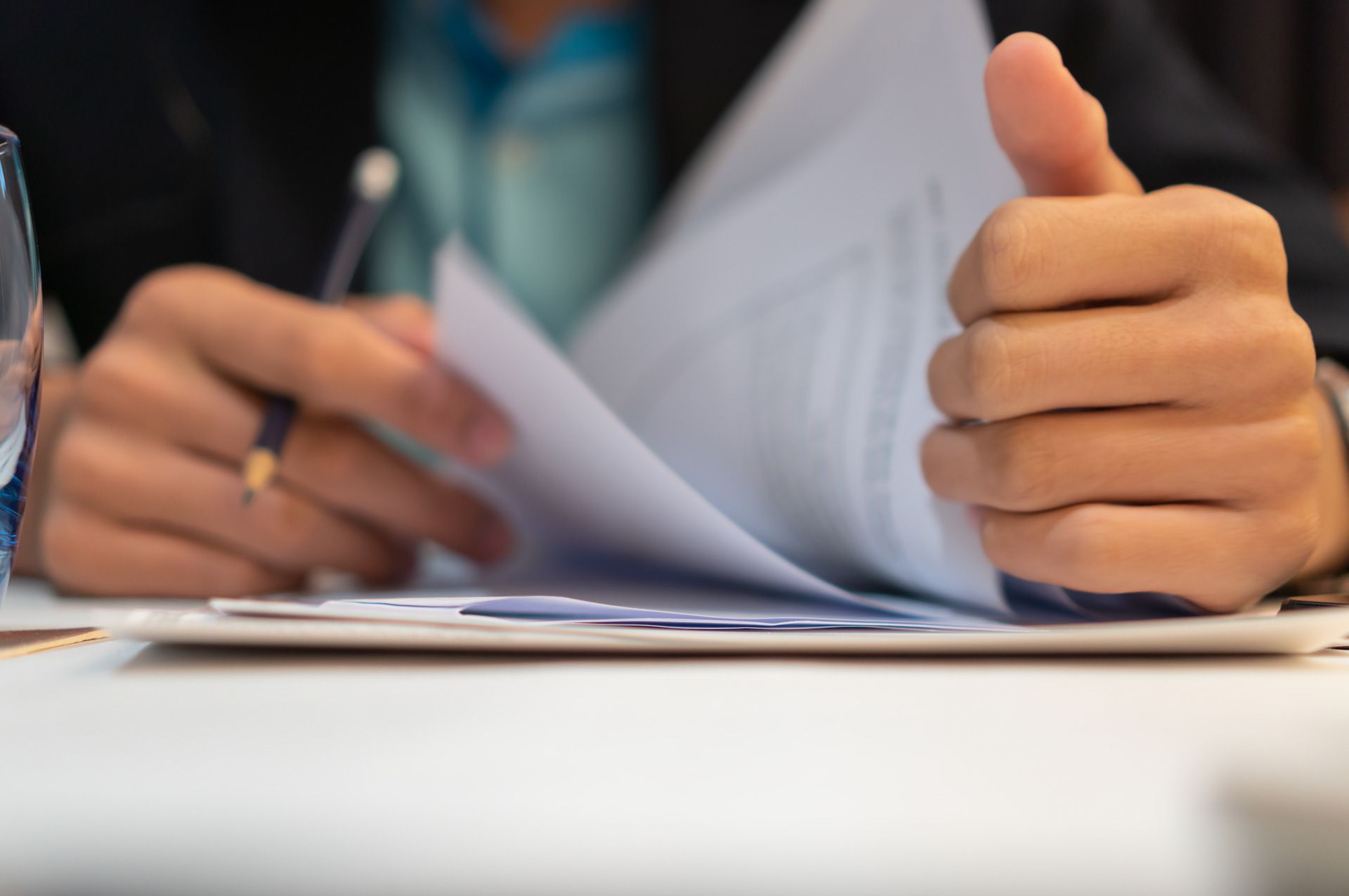 A person is sitting at a table holding a piece of paper and giving a thumbs up.