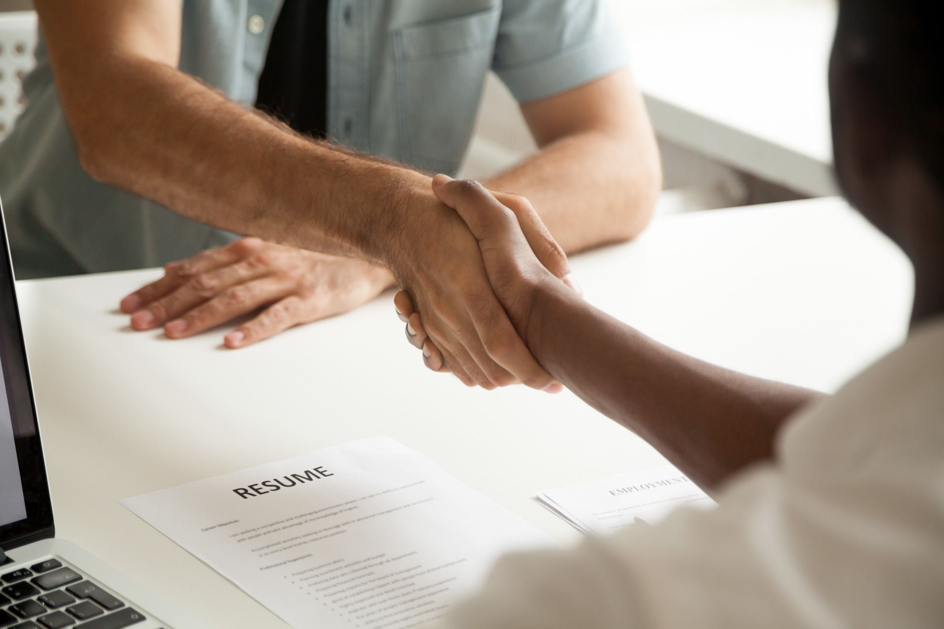 Two men are shaking hands over a resume.