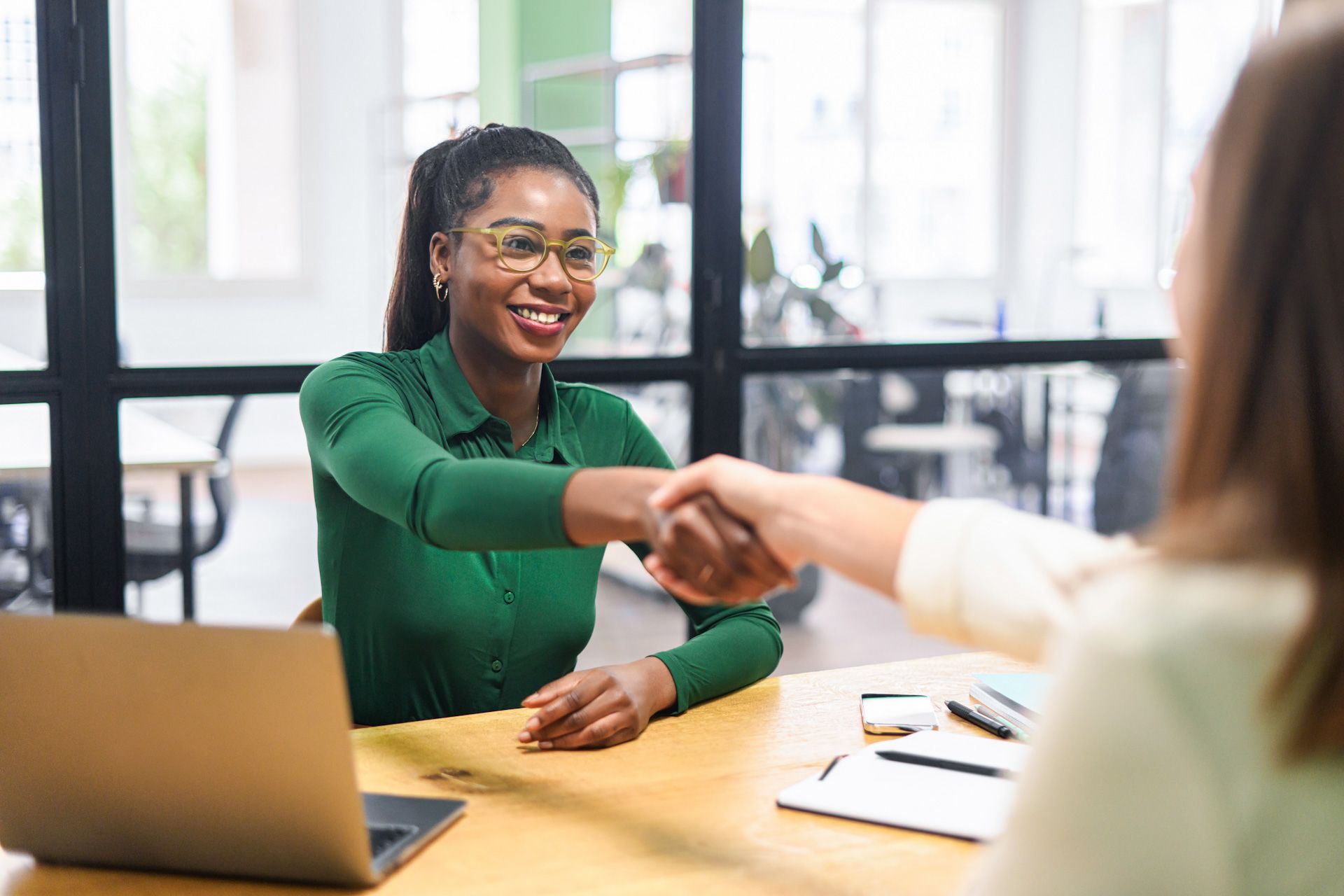A woman in a green shirt is shaking hands with another woman at a table.