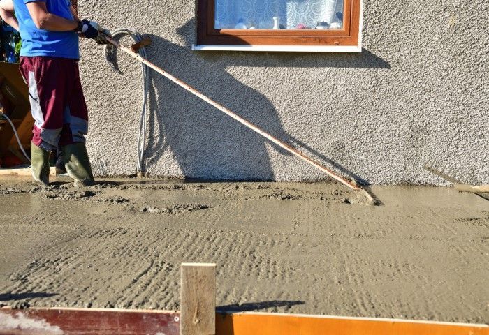 Worker bull floating new concrete slab beside stucco wall in Bushnell