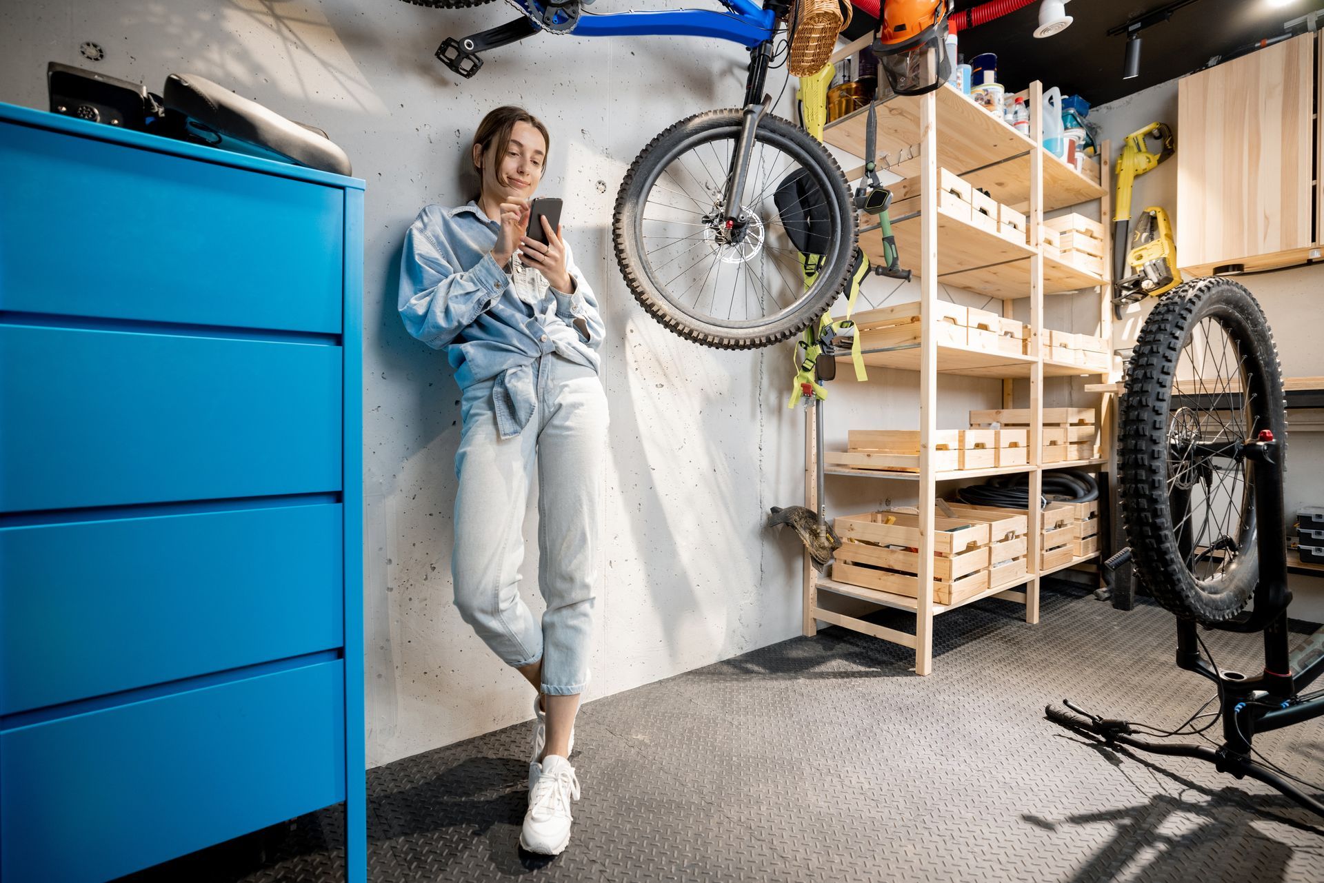 A woman is leaning against a wall in a garage while looking at her phone.