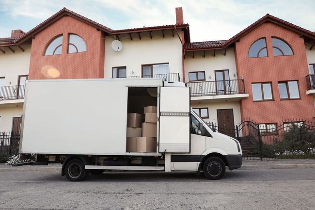 A white moving truck is parked in front of a large brick house.