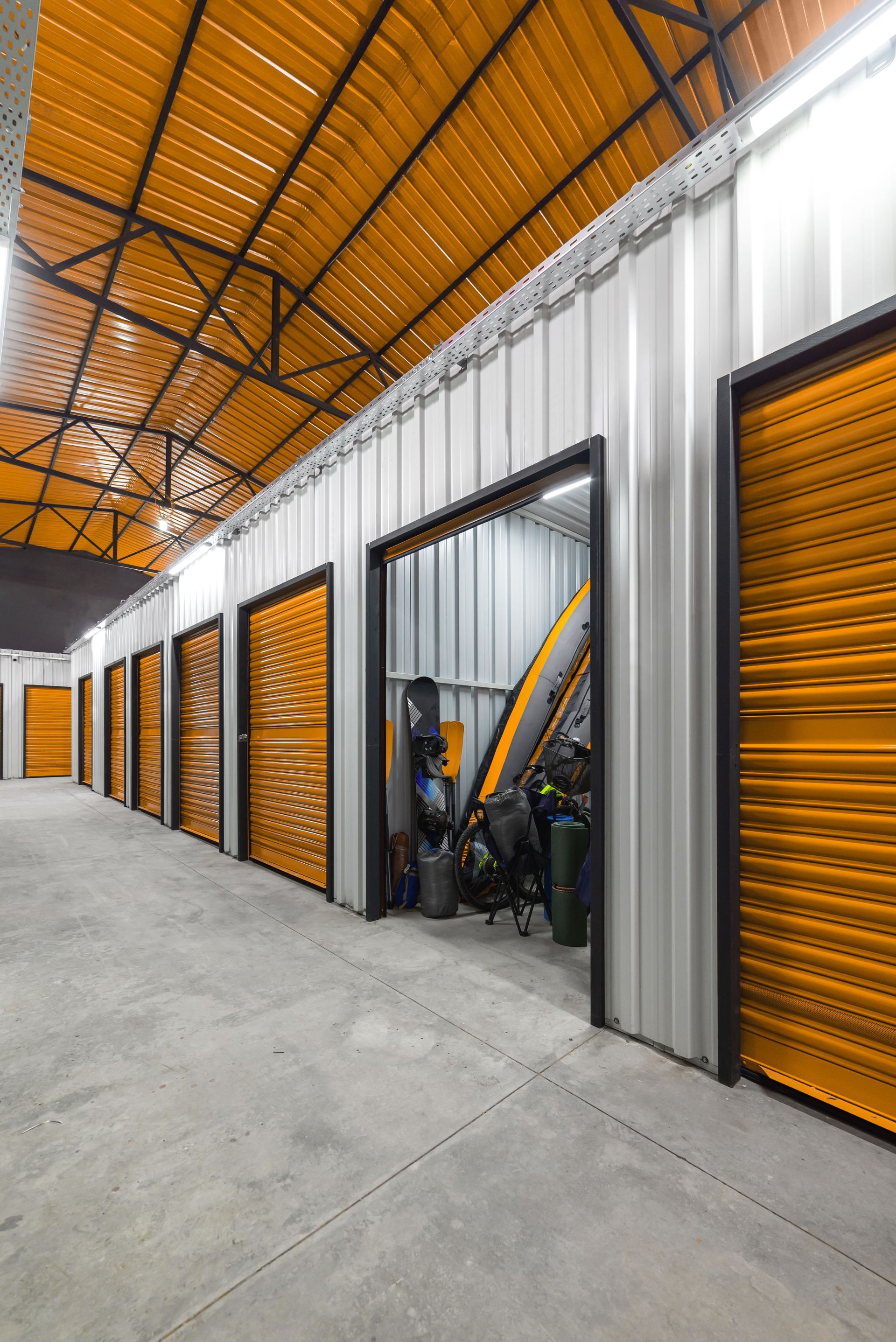A row of storage units with orange doors and a yellow roof.