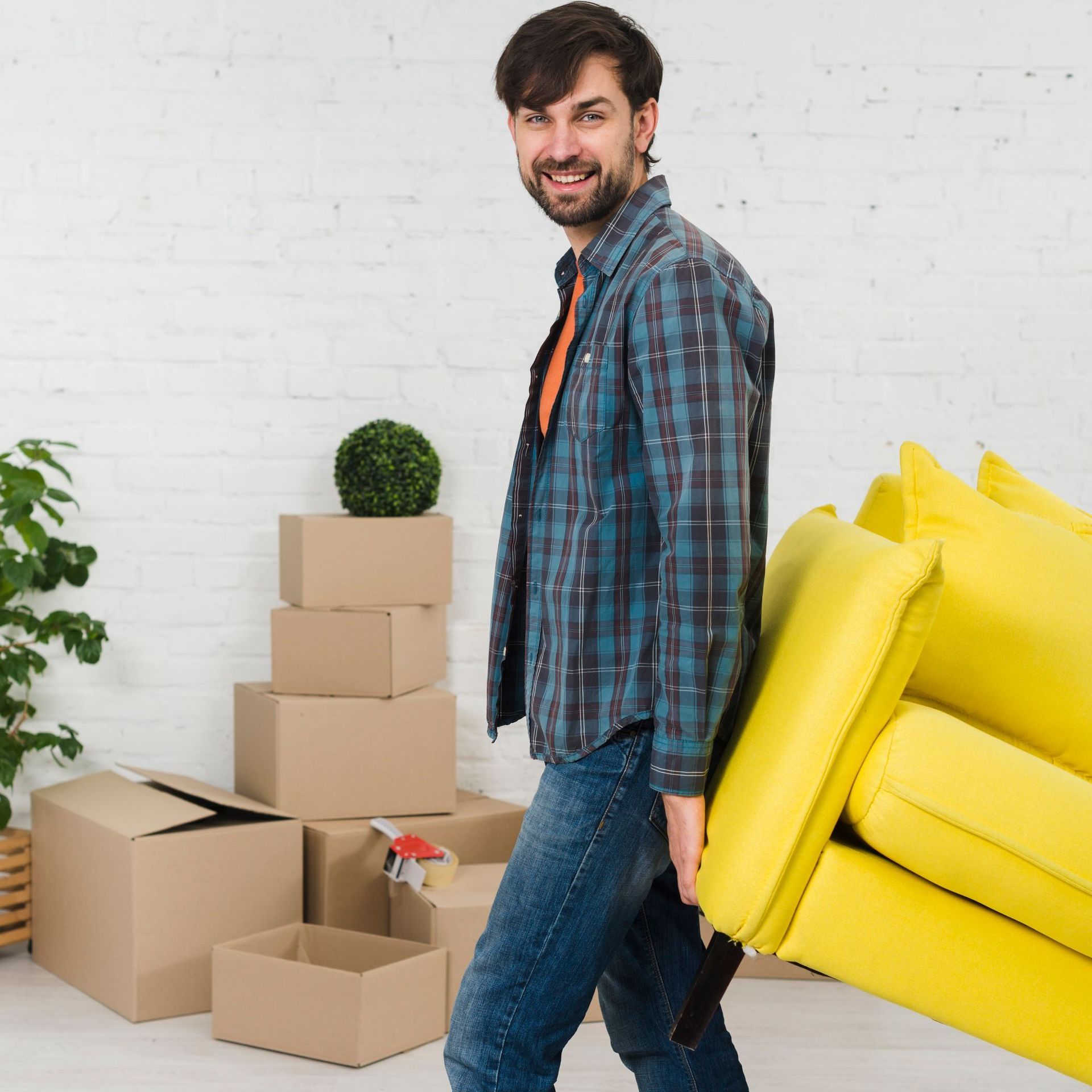 A man is carrying a yellow couch in a living room.