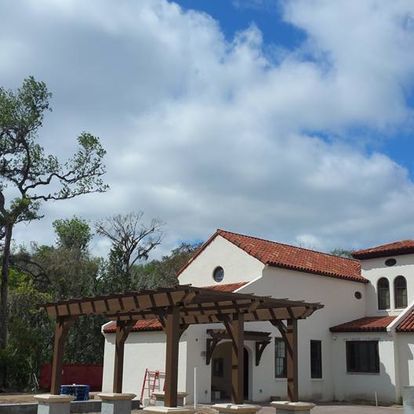 A white house with a red tile roof and a wooden pergola