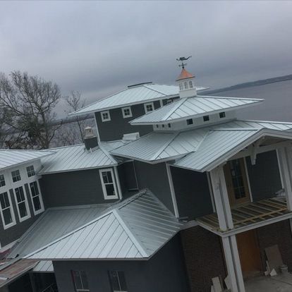 A large house with a metal roof and a weather vane on top.