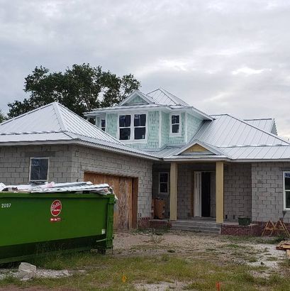 A large house under construction with a green dumpster in front of it