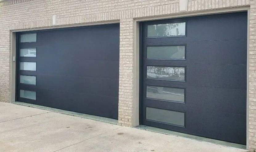 Two black modern garage doors with rectangular glass panels, set in a brick facade.