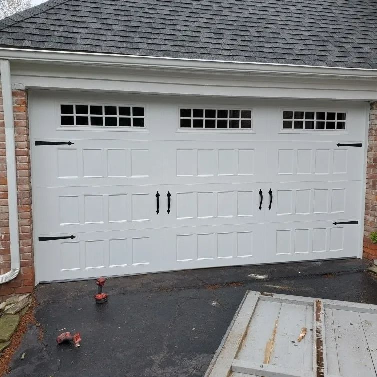 White garage door with decorative black hardware and rectangular windows along the top.