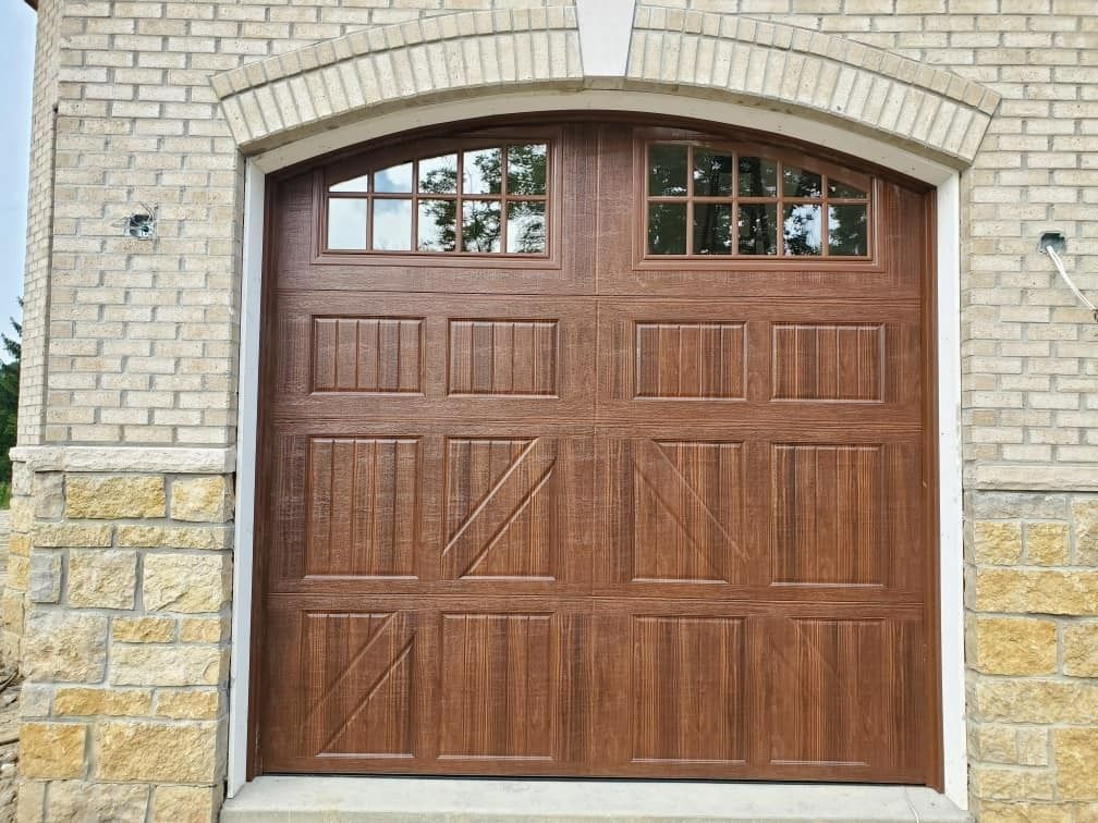 Brown garage door with arched window, brick and stone facade.