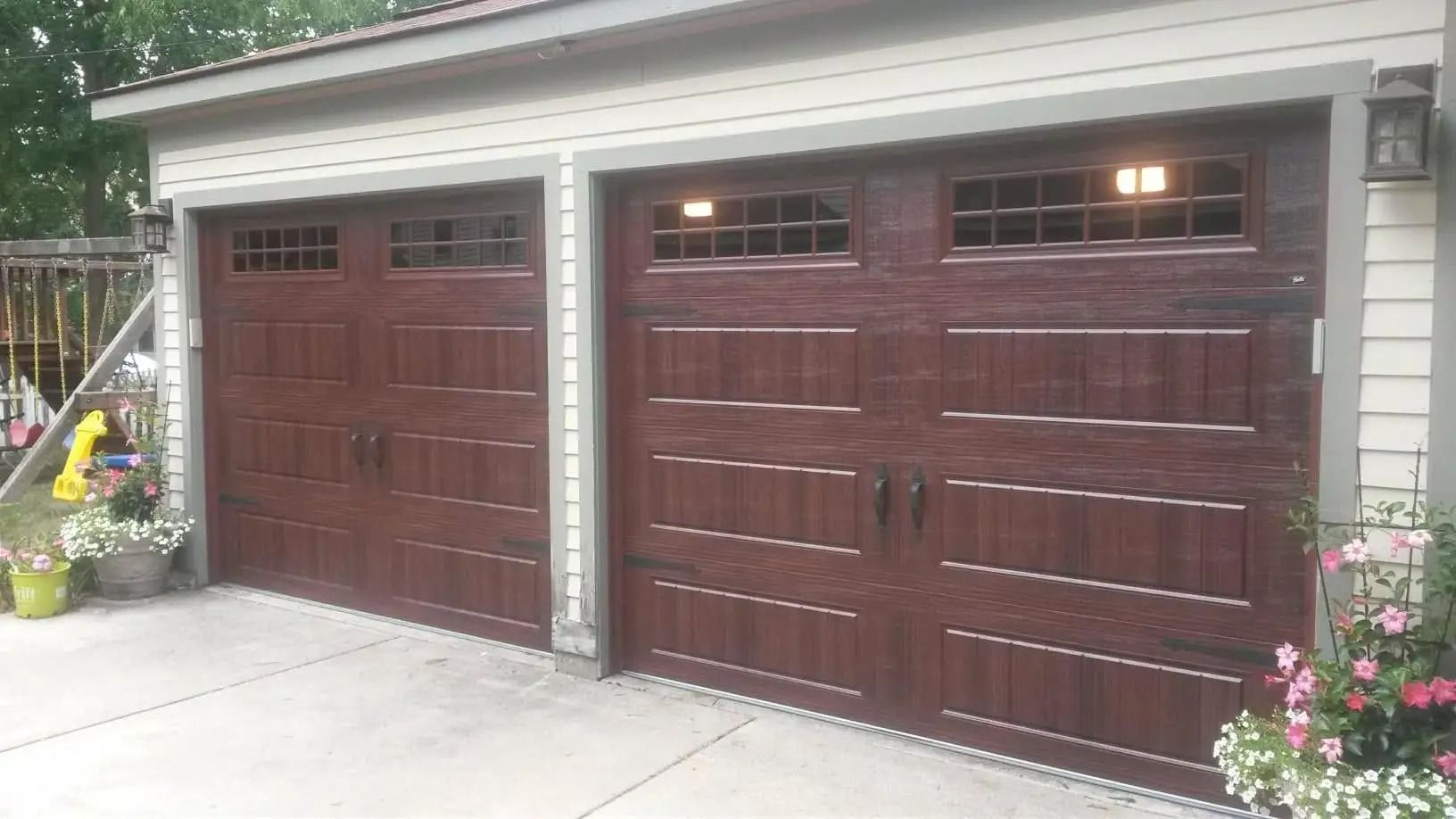Two dark brown garage doors with windows, set in a concrete driveway.