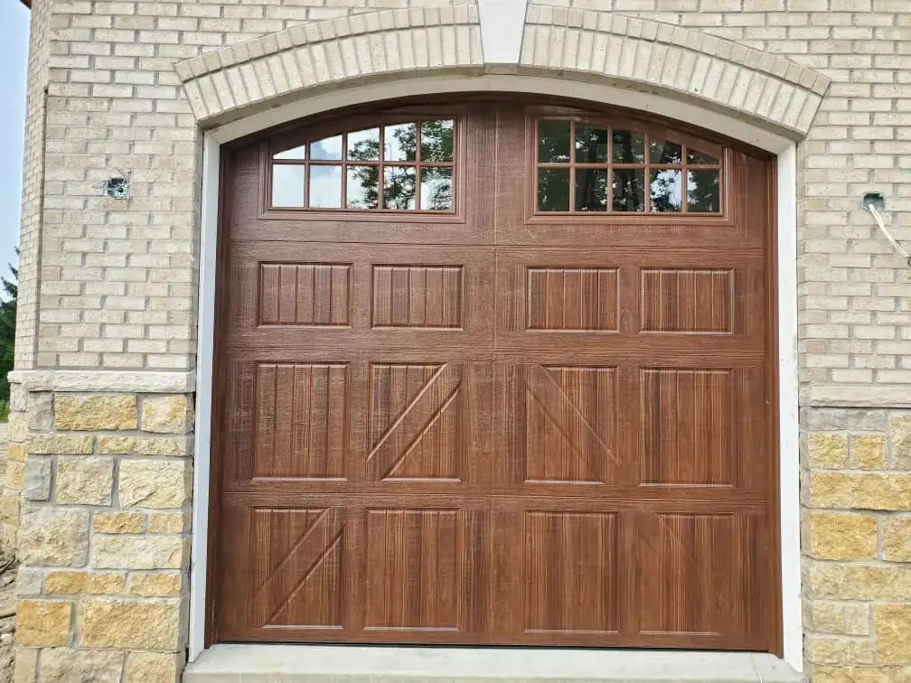 Brown garage door with arched top and windows, set in a brick and stone facade.