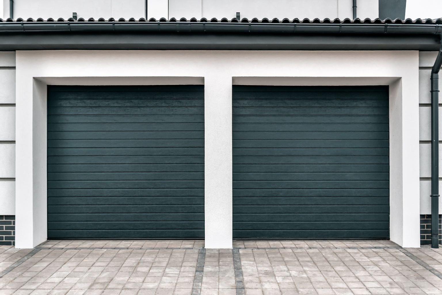 Two gray garage doors framed by white trim and a brick driveway.