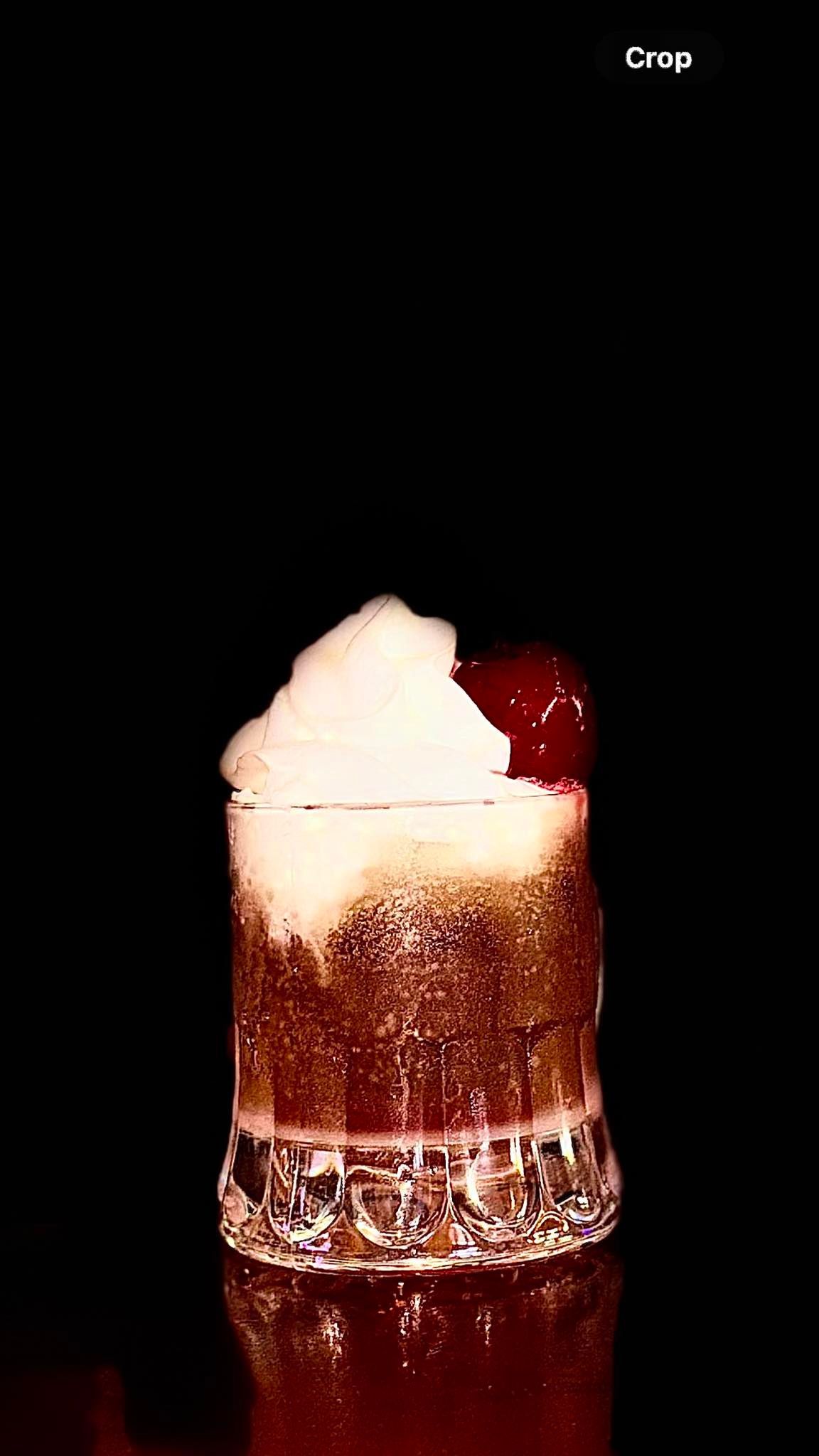 Cocktail with froth and a cherry, against a black background.