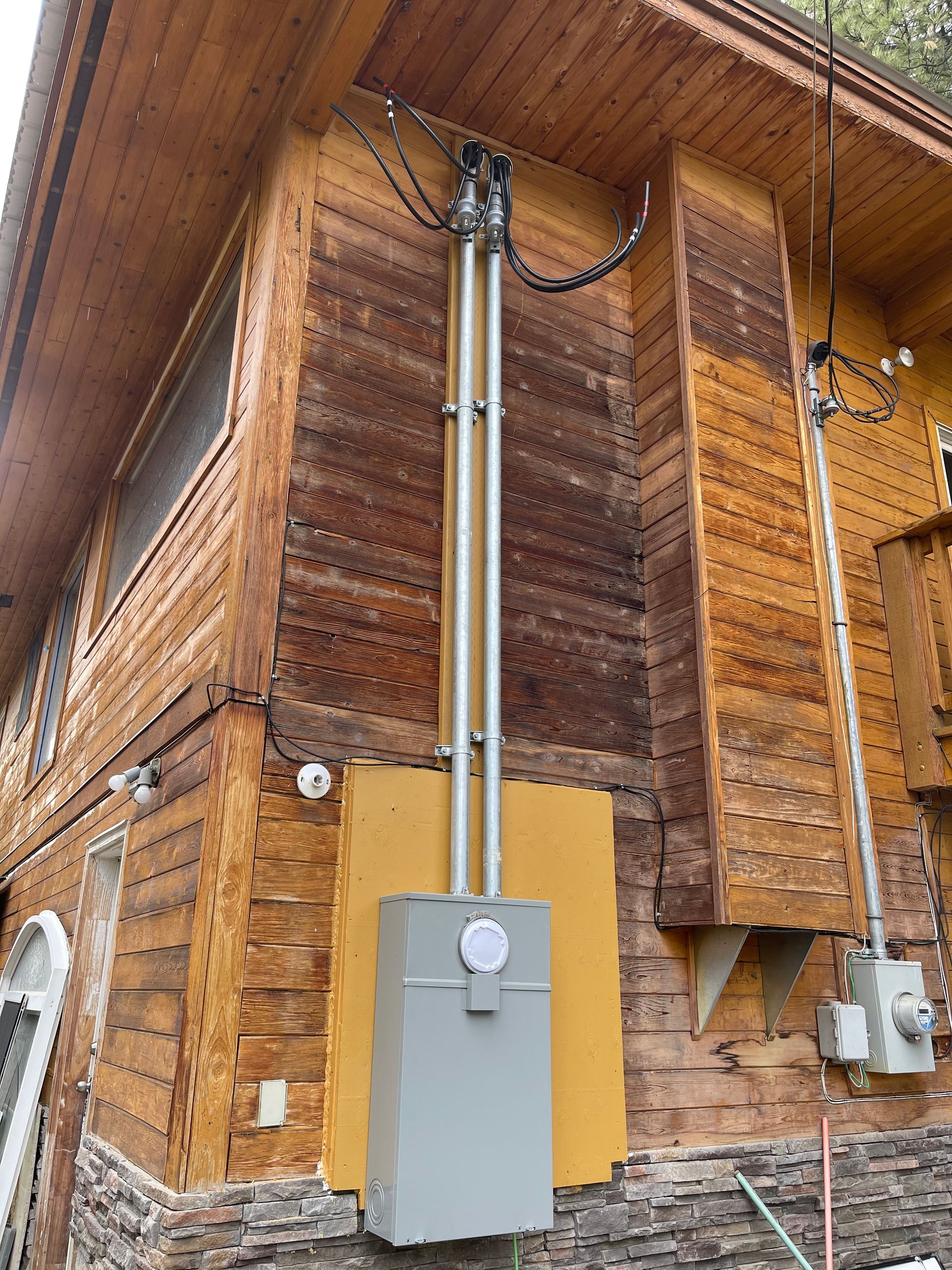 Exterior view of a house with a new electrical meter box and conduit installed on the wooden wall.