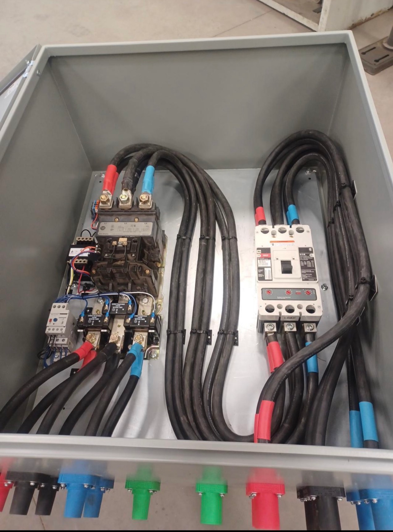 Electrical panel with black cables, circuit breakers, and color-coded wires inside a gray enclosure.