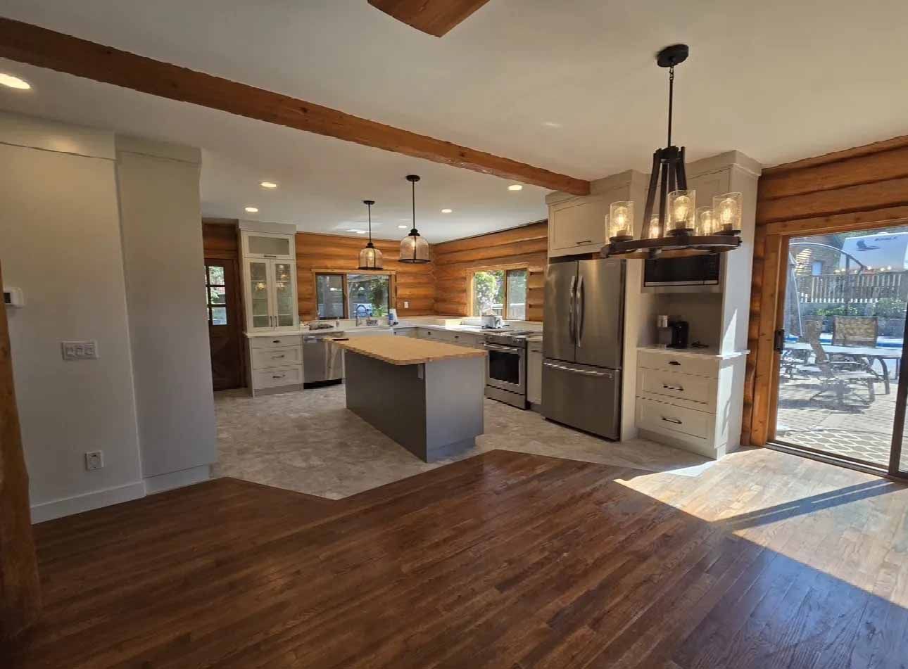 Spacious kitchen with log walls, gray island, stainless steel appliances, and sliding glass door to a deck.