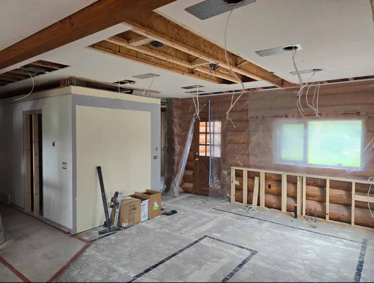 Interior of a room under renovation; exposed wooden beams, walls, and ceiling. Insulation visible; electrical wires hanging.
