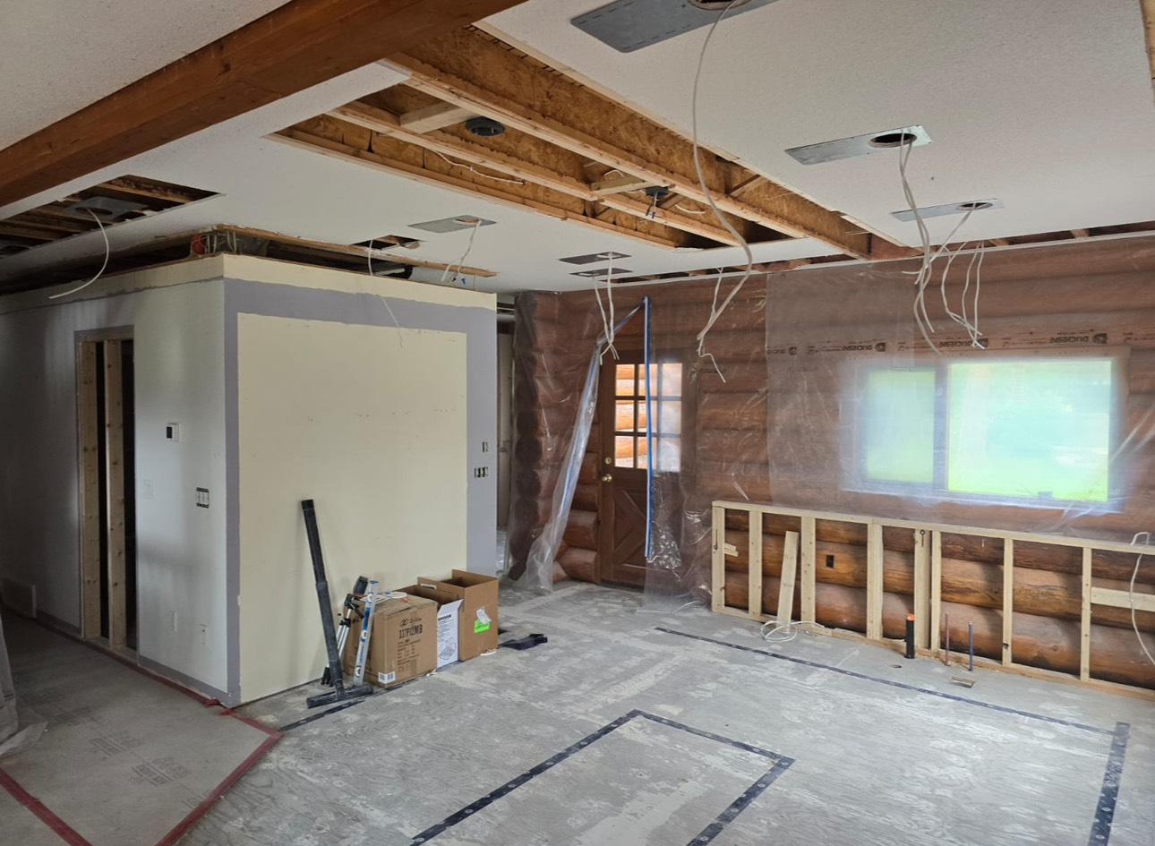 Interior of a room under construction. Exposed beams and wiring, unfinished walls, and debris on the floor.