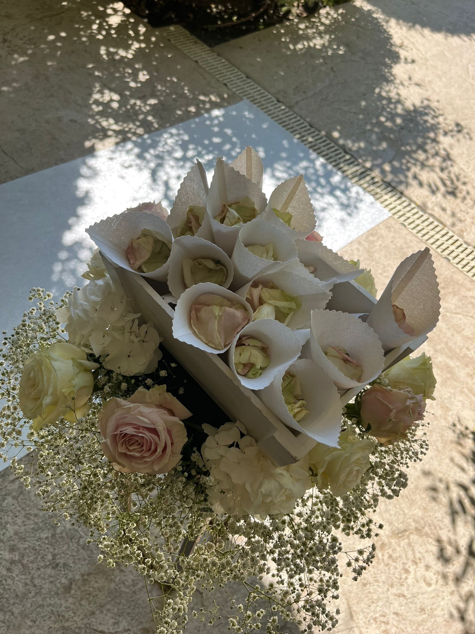 Coni di coriandoli in una scatola bianca, circondati da fiori, su una superficie chiara.