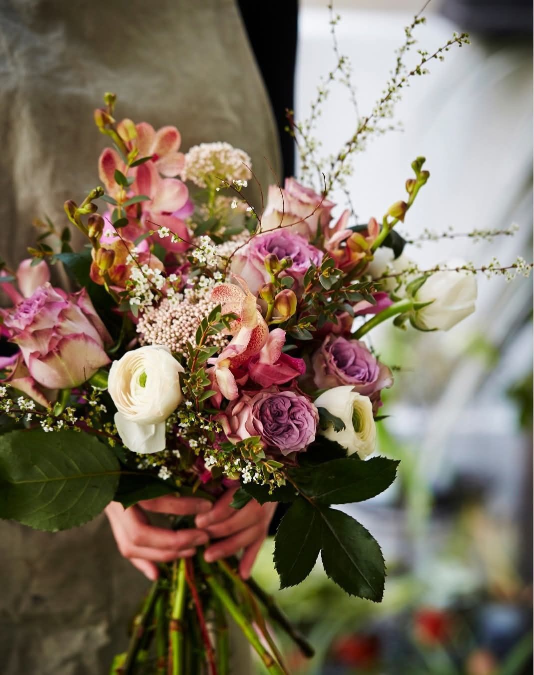 Persona che tiene in mano un mazzo di fiori rosa, viola e bianchi con del verde, in un negozio.