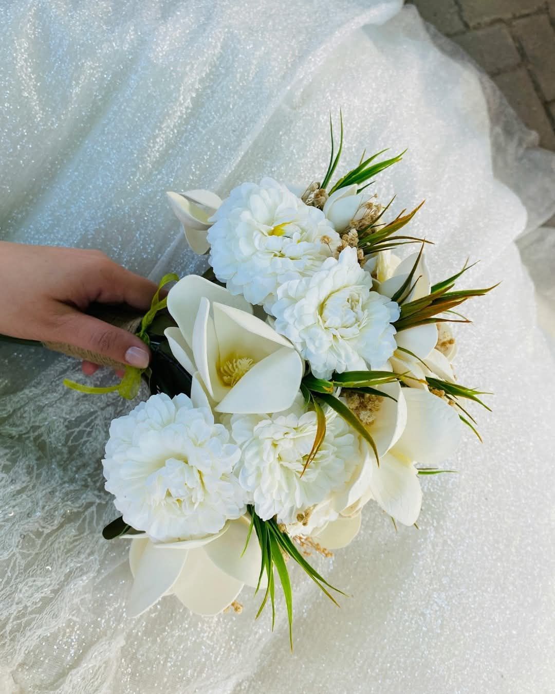 Mano che regge un piccolo bouquet di fiori bianchi su un vestito bianco.