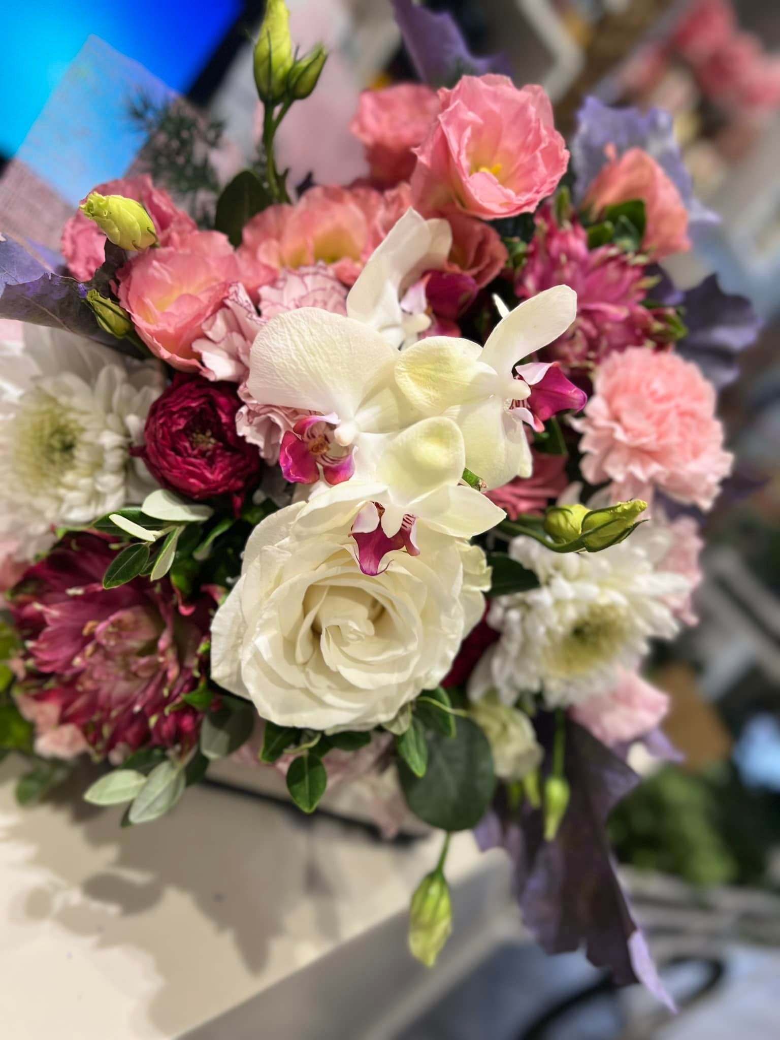 Primo piano di un bouquet con fiori rosa, bianchi e bordeaux. Alcuni sono circondati da foglie verdi.