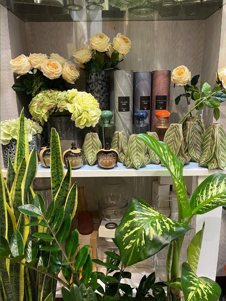 Esposizione di bouquet, vasi e piante verdi in un negozio di fiori. Include rose, ortensie e foglie decorate.