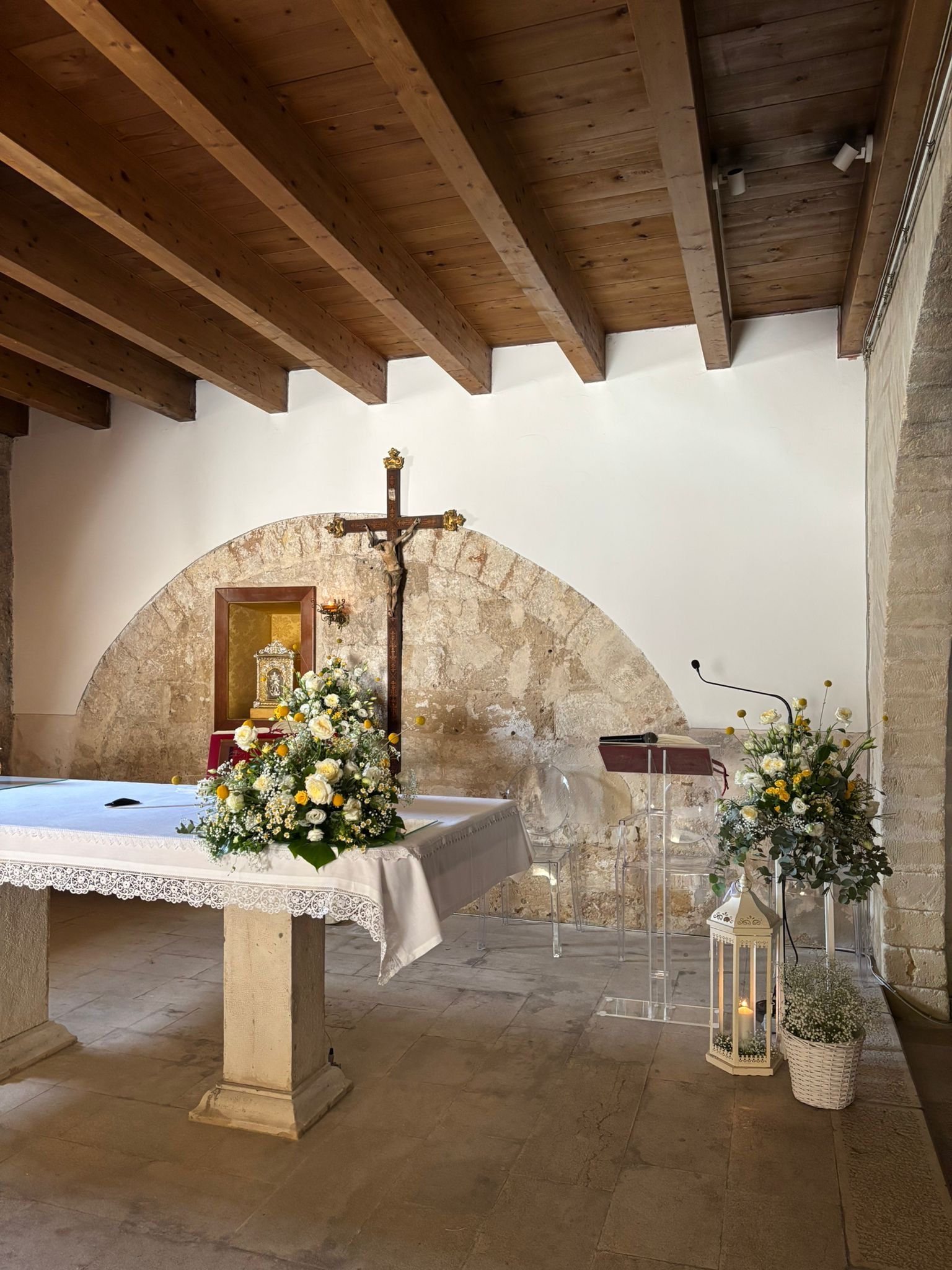 Un altare con fiori e un crocifisso, all'interno di una cappella in pietra.