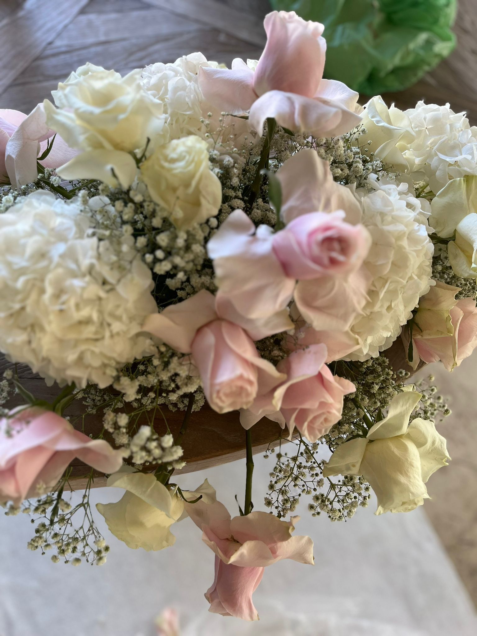 Primo piano di un bouquet con garofani bianchi, rose rosa e piselli odorosi giallo pallido, disposti su una superficie di legno.