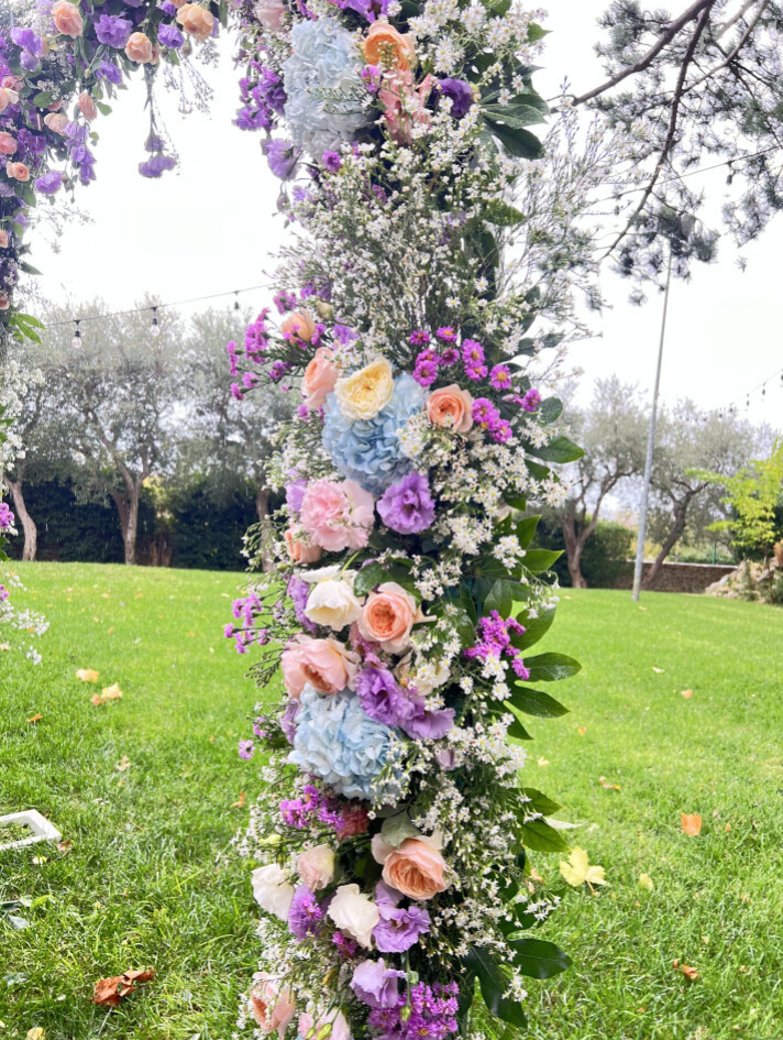 Candela bianca all'interno di una lanterna decorativa, circondata da fiori bianchi e verde.