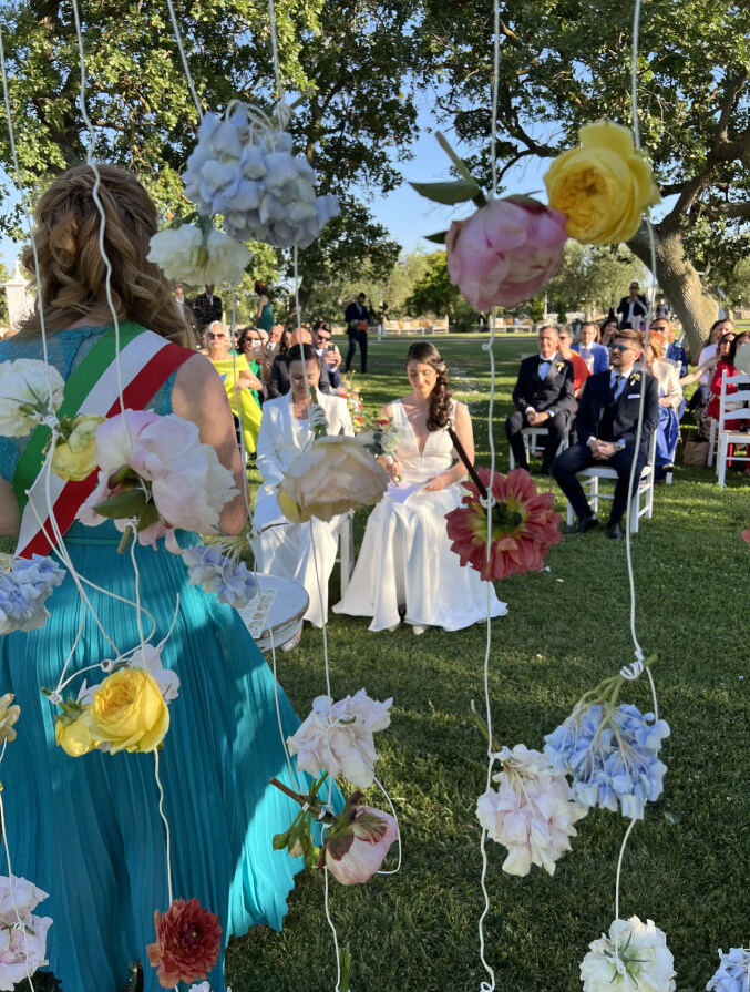 Cerimonia nuziale all'aperto con composizioni floreali su sedie e un paesaggio erboso.