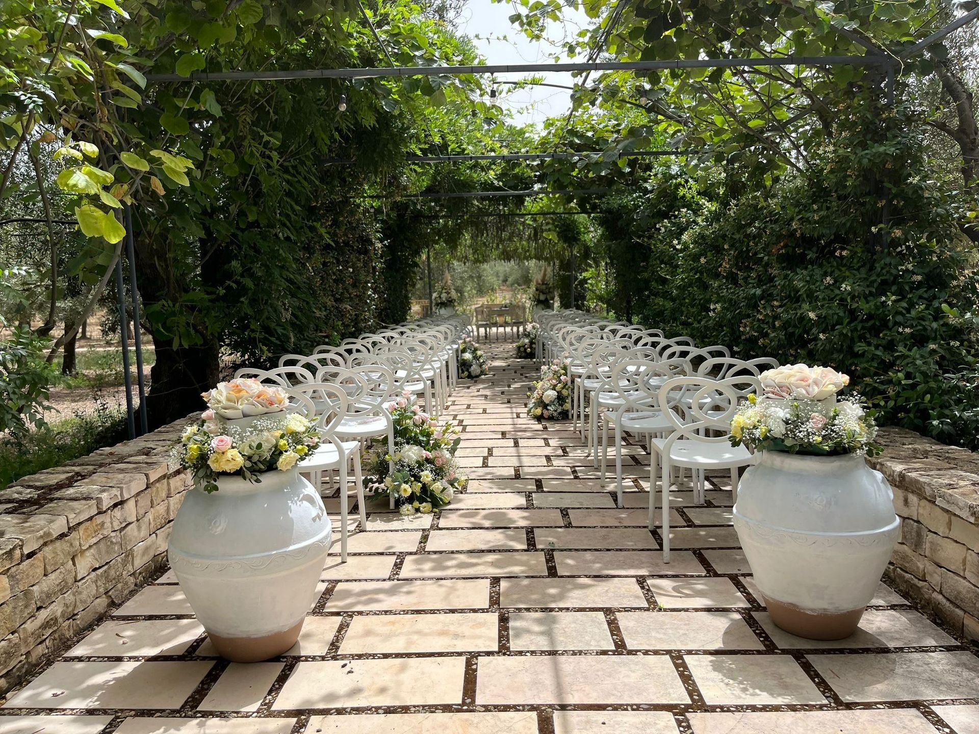Allestimento per la cerimonia nuziale con sedie bianche, composizioni floreali e un baldacchino verde.