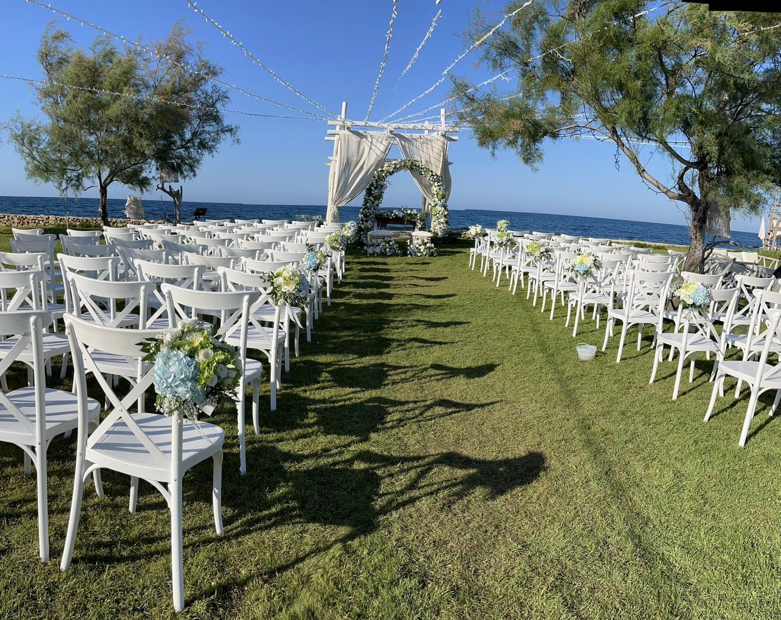 Cerimonia nuziale allestita all'aperto con sedie bianche, arco floreale e bandiere su un prato erboso.
