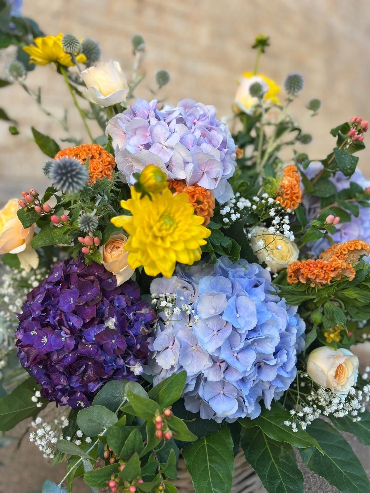 Composizione floreale colorata con ortensie viola, blu e gialle, cardi e bacche arancioni.