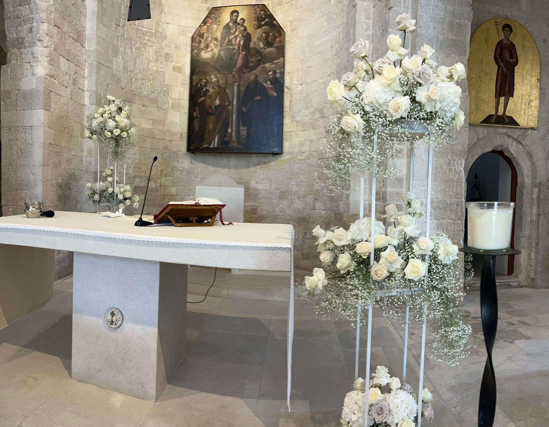 Altare della chiesa decorato con fiori bianchi per una cerimonia. Sono visibili muri in pietra e un dipinto.