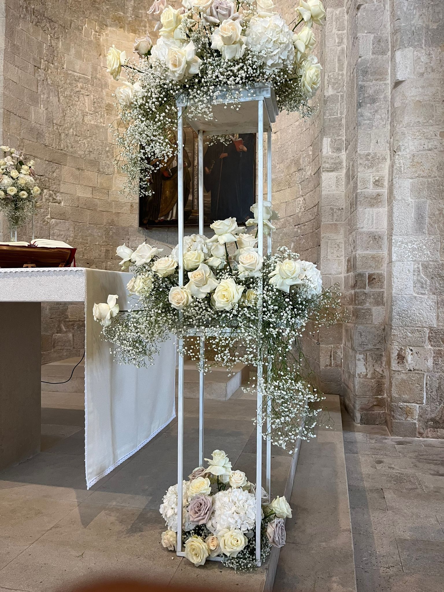 Composizione floreale bianca su un supporto metallico a più livelli in una chiesa.