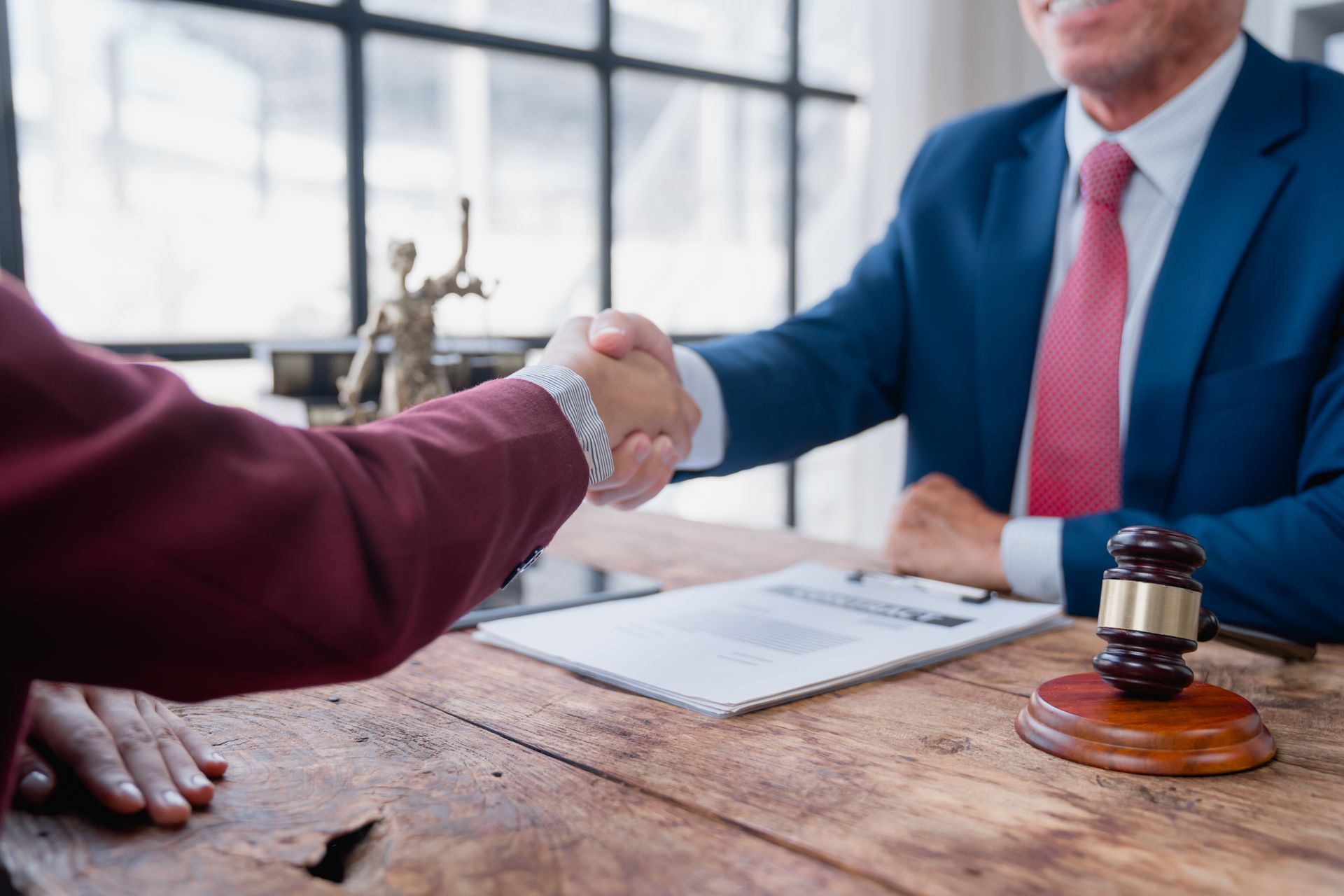 Handshake across a desk during a legal agreement, with documents and a gavel visible