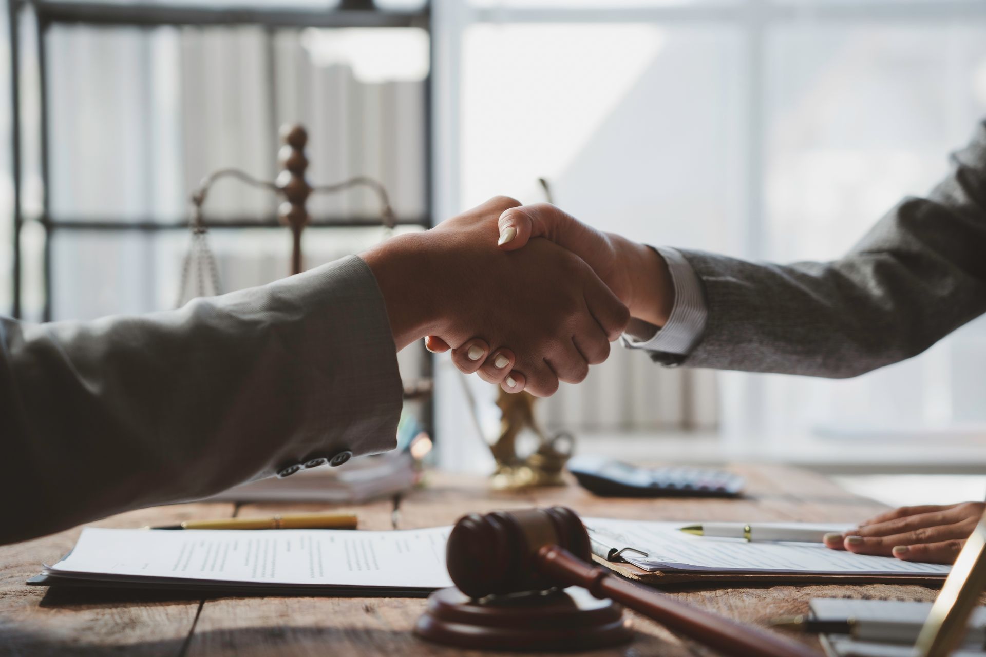 Two people shaking hands across a desk in a bright office, with documents and a gavel nearby.