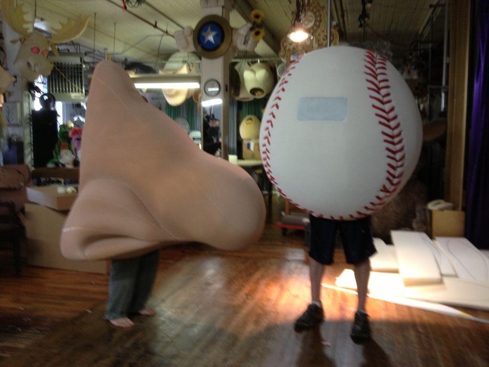 A man holding a giant nose and a baseball