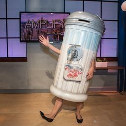 A woman in a trash can costume is standing in front of a television.