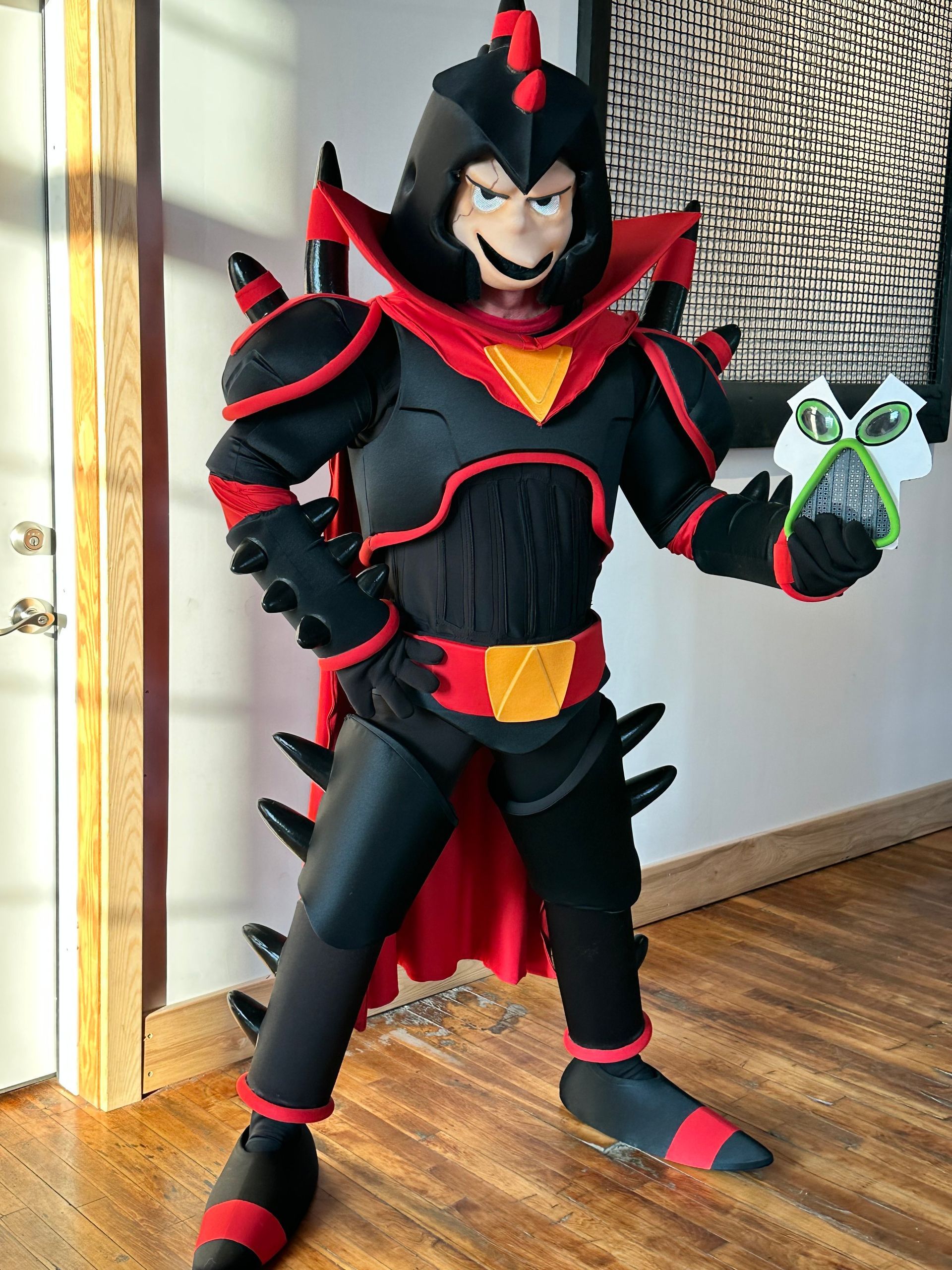 A person in a black and red costume is holding a green object.